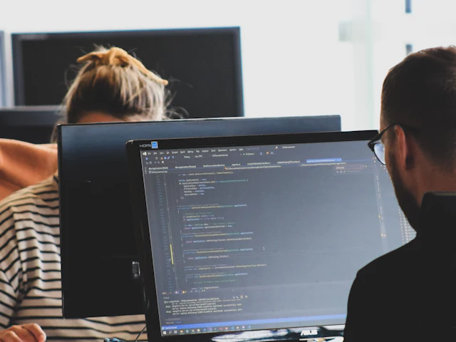 Two developers reviewing code on large monitors in a bright office